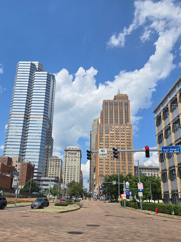 A shot from the intersection of a street in Pittsburgh, PA. Brick roads lined with skyscrapers are in view.