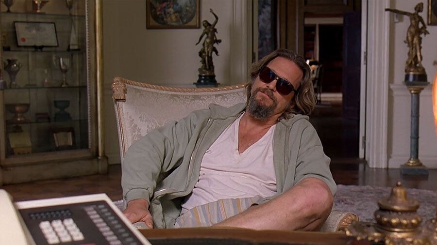 Image shows The Dude, from The Big Lebowski, who is sitting in a chair with his legs crossed. His body language is somewhat un dude but he’s upset because people pissed on his rug. It really held the room together. 