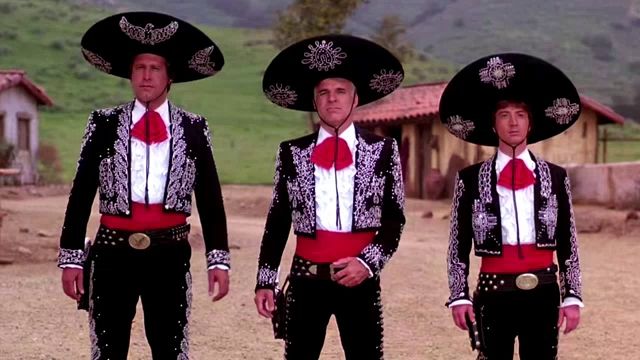 three men dressed as mariachis stand in a dirt field