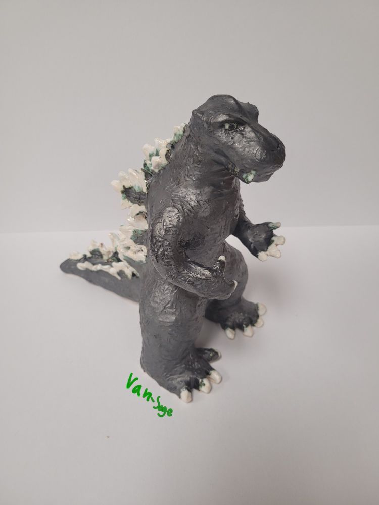 A shiny, ceramic Godzilla is on a white sheet of paper.