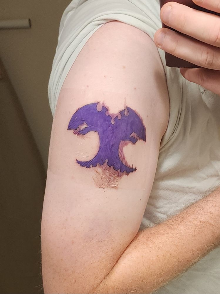 A fresh tattoo of the Tyranid army symbol on my shoulder. It's got a thin plastic film to protect it, and there's blood seeping from the tattoo underneath. 