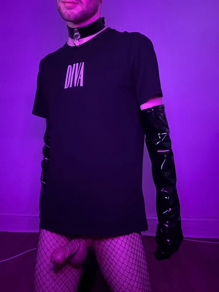 A man kneeling in front of the camera in fishnets, black boots, gloves, a collar, and a black t-shirt with ‘Diva’ on the front.