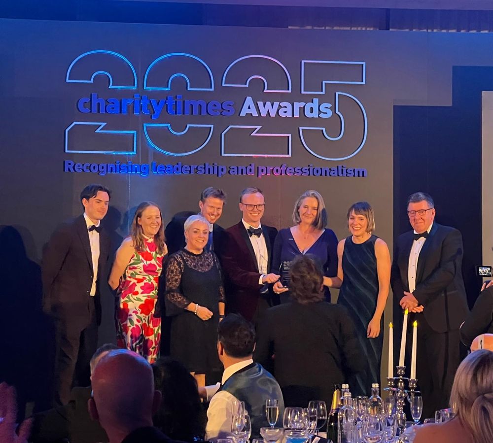 A group of people standing in front of the Charity Times 2025 Awards sign, dressed in black tie