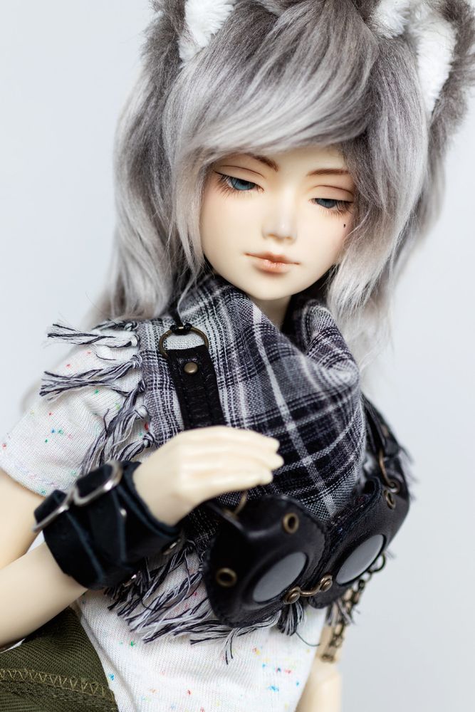 Amaretto Biscotti (Alchemic Labo Decadent B-el) wears green coveralls, a speckled t-shirt, a gray plaid scarf, and black leather accessories. His gray faux fur wig has large upright wolf ears. His demeanor is cool and confident.