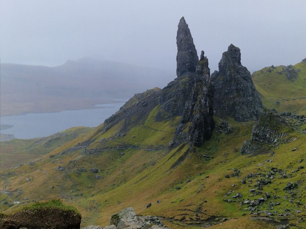 Blick vom Plateau, von oben auf die Felsformation Old Man of Stor, die sich wie felsige Nadeln aus grünem Grund erheben.