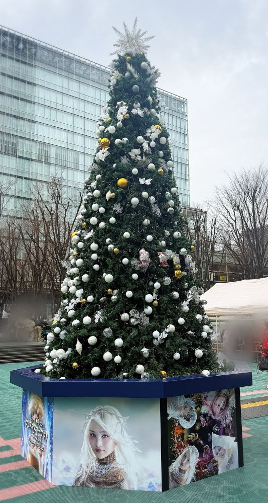 広場に設置されているクリスマスツリー。白と銀、時々金の飾り付けがされてる。土台にはももクロライブのキービジュアル。