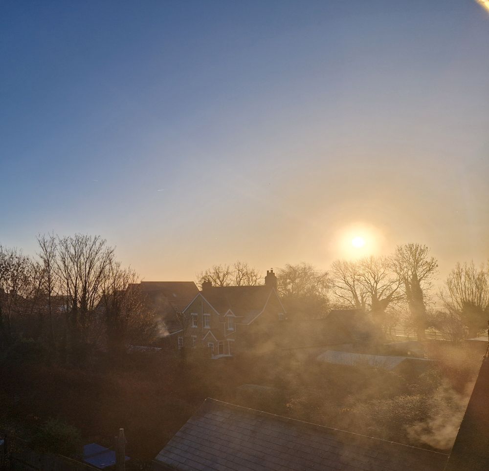 Winter morning view from bedroom window over rooftops and back gardens. Low winter sun trying to burn off the mist. Glowing golden.