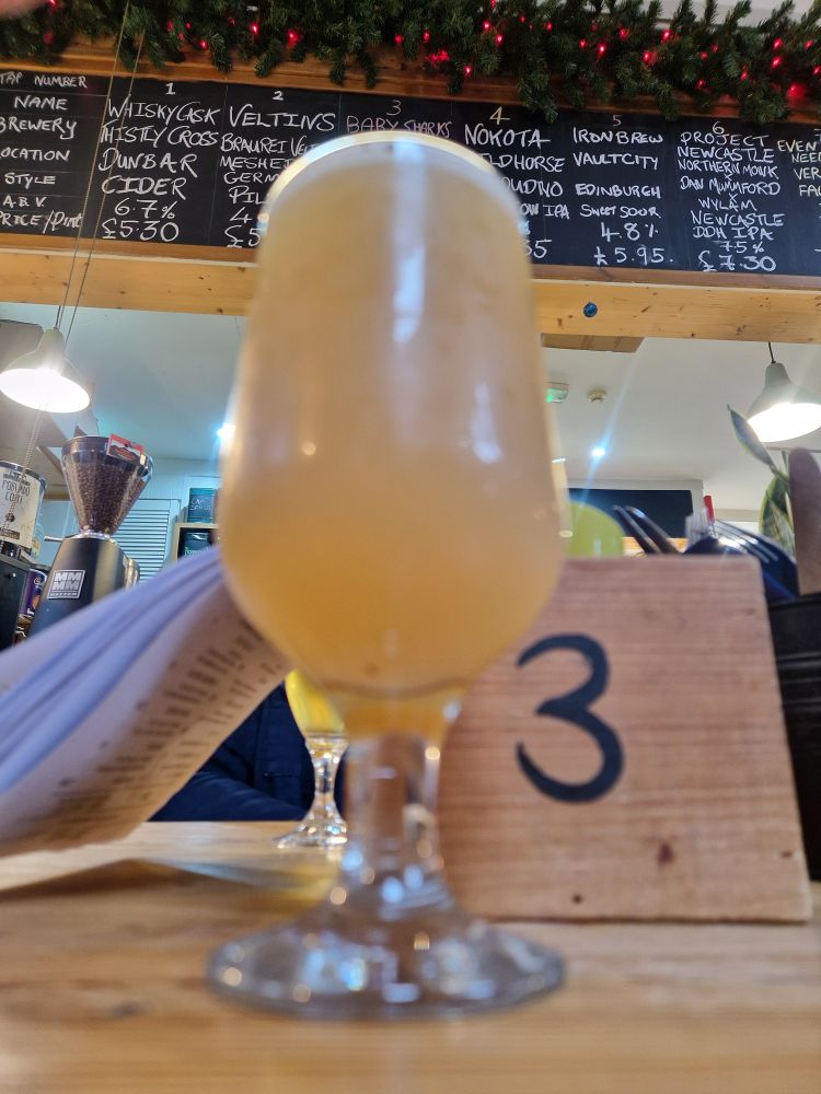 Schooner of excellent IPA with beer menu on blackboard in background