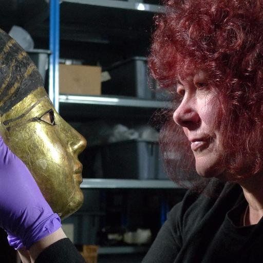 Photograph of Professor Joann Fletcher holding Wigan Museum's 18th dynasty gilded coffin face. Joann is pictured looking into the eyes of mask, as if it is reflected in a mirror.