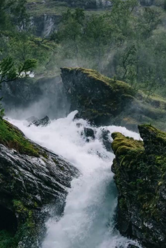 a waterfall is surrounded by rocks and trees in a forest