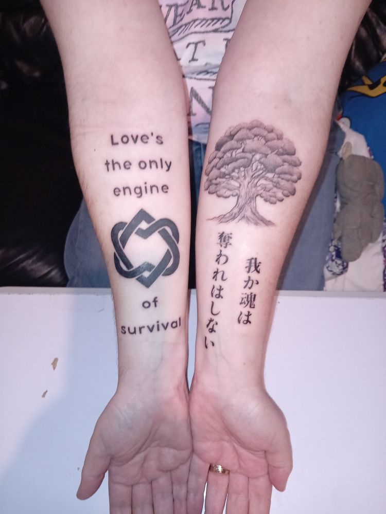 My inner forearms, both bearing fresh tattoos. The right arm has Leonard Cohen's Unified Heart symbol and a line from his song The Future: "Love's the only engine of survival." The left arm has a picture of one of the 500-year-old camphor trees that survived the atomic bombing of Nagasaki, with a line from Fukuyama Masaharu's song Kusunoki (Camphor Tree): 我が魂は 奪われはしない (my soul will never be taken away).