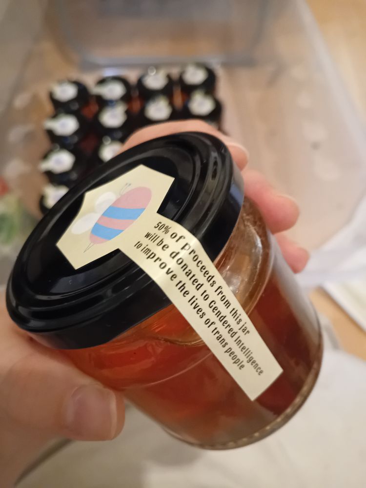 The tamperproof sticker on a jar, which reads, "50% of proceeds from this jar will be donated to Gendered Intelligence to improve the lives of trans people."