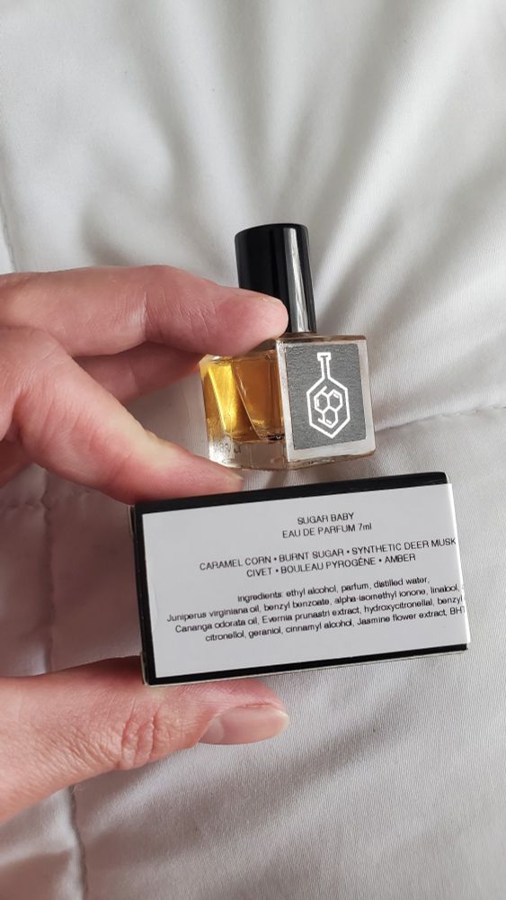 Gwyn's hand holding a little bottle of perfume and the box showing it is named Sugar Baby 