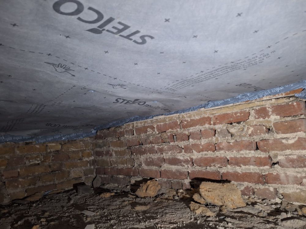 Vapour permeable membrane stuck under the wood fibre insulation under a wooden suspended floor. Picture taken in the crawl space beneath, full of dirt and detritus.