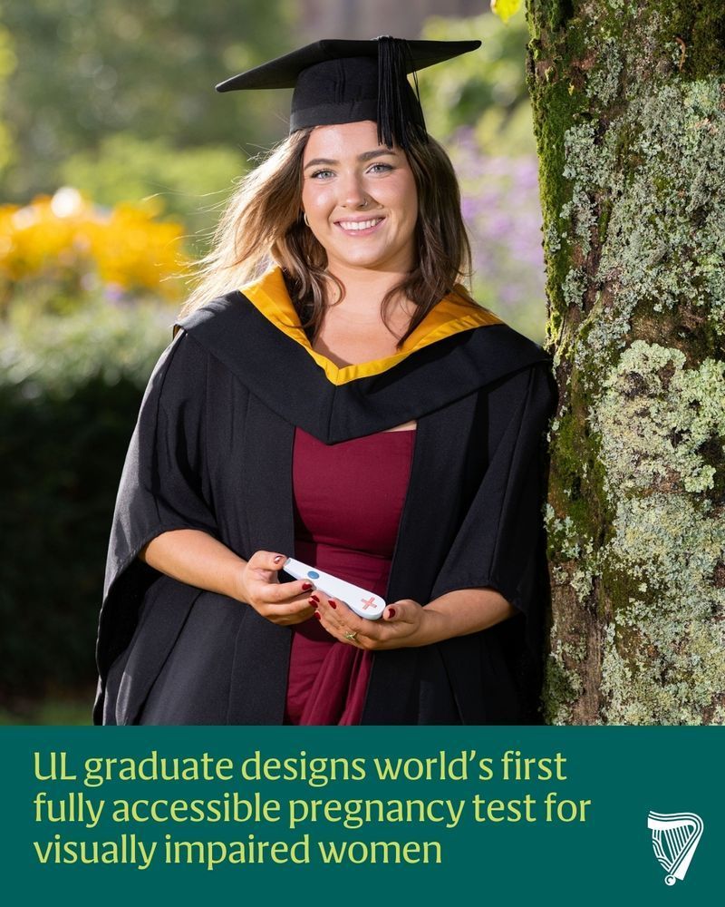 A photo of Leah wearing a graduation robe and cap, holding an example of the Amy pregnancy test. It's handheld plastic device with a tactile plus symbol on one end and a button on the other. The caption reads: UL graduate designs world’s first fully accessible pregnancy test for visually impaired women