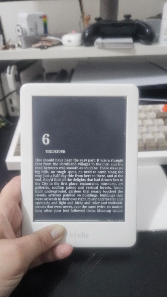 imagem de um kindle 10 geração branco, com um livro aberto, o fundo é preto e a fonte branca. 