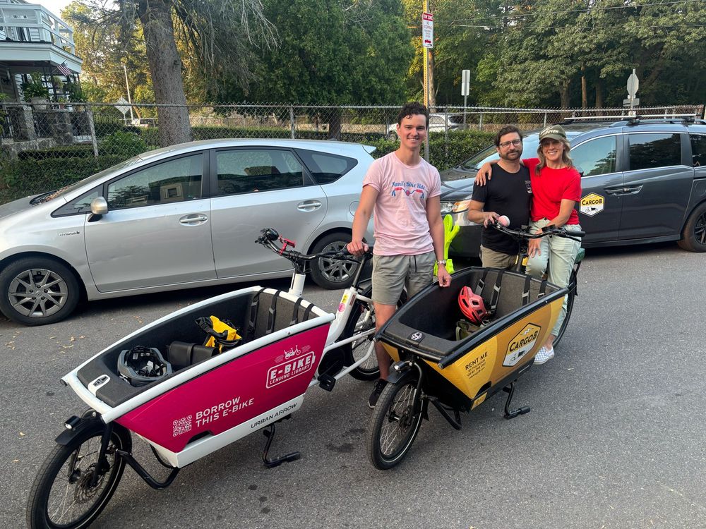Three neighbors standing behind two Urban Arrow cargo bikes. One branded for the company “CargoB” and the other for “E-Bike Lending Library