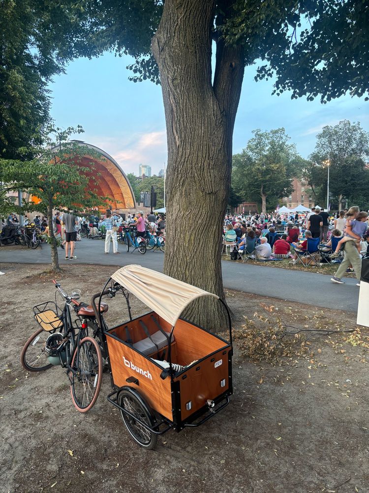 Bunch trike parked in front of a tree with a crowd in the back