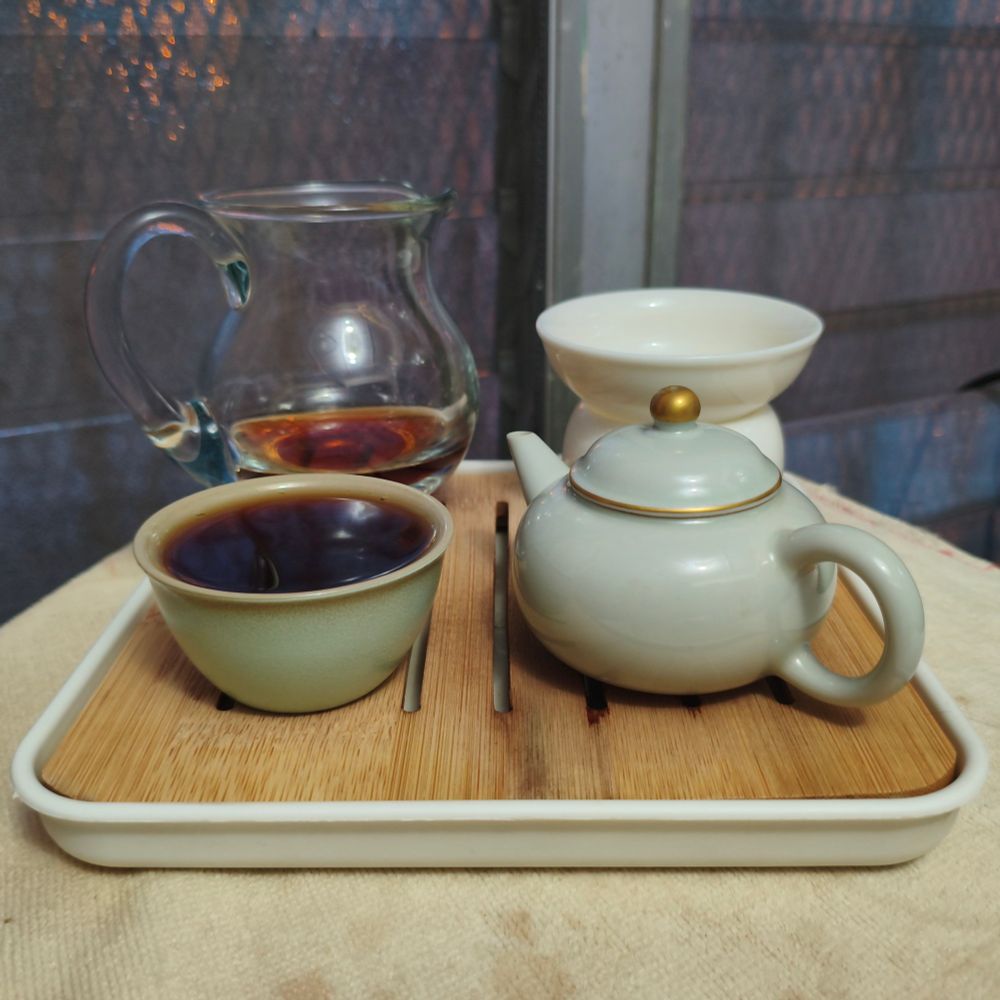 A tray with the following items on it: a cup of tea, a teapot, a glass pitcher, and a ceramic strainer.