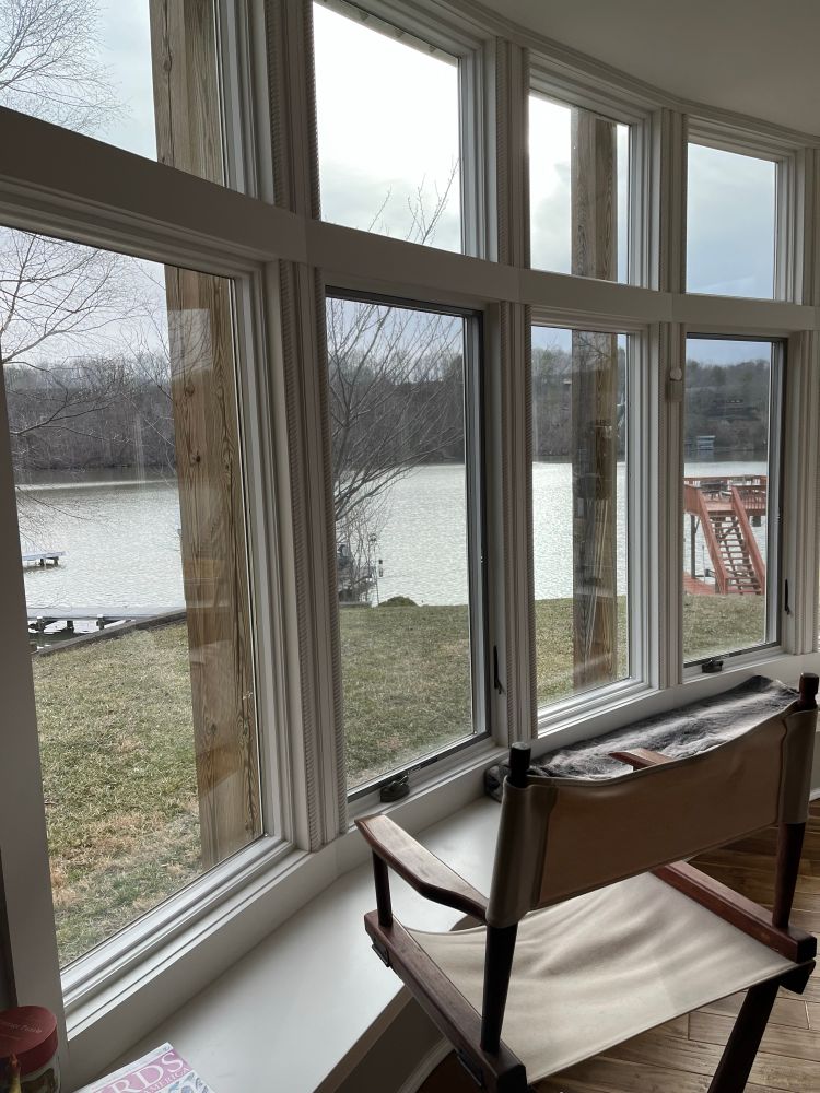 An empty chair in front of a bank of windows. Outside the windows, an overcast view of a lake with docks in the background. An invitation to sit and enjoy the view…