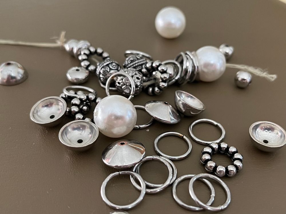 Photo of a broken bracelet. Shiny silver beads, rings, and pearls of various sizes are scattered against a flat brown background. A few pieces in the background are still attached to the broken string.