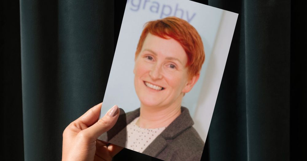 A picture of a hand holding a photo of Wendy against a green curtain