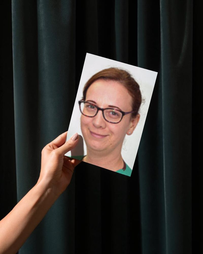 A picture of a hand holding a photo of Lynne against a green curtain