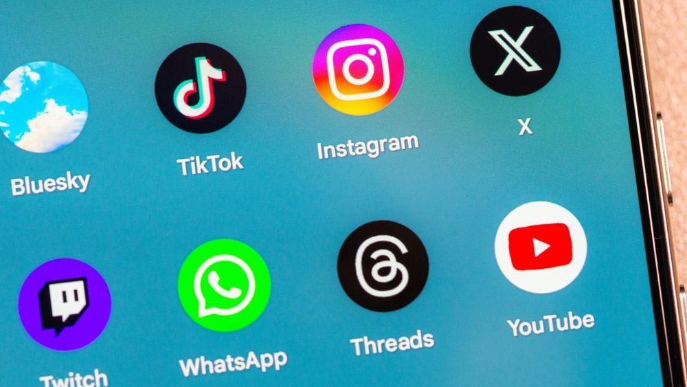 A phone screen displaying various social media apps on it including Bluesky, Tiktok, X, Instagram, WhatsApp and more.
