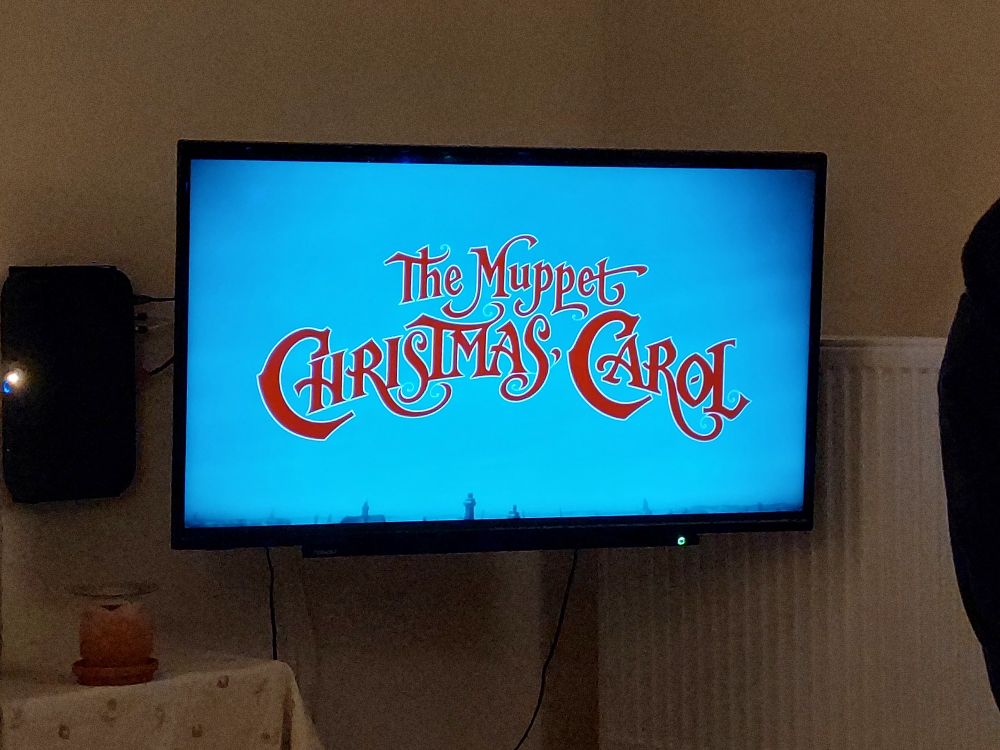 A picture of the title card from "The Muppets Christmas Carol" being watched on a TV.