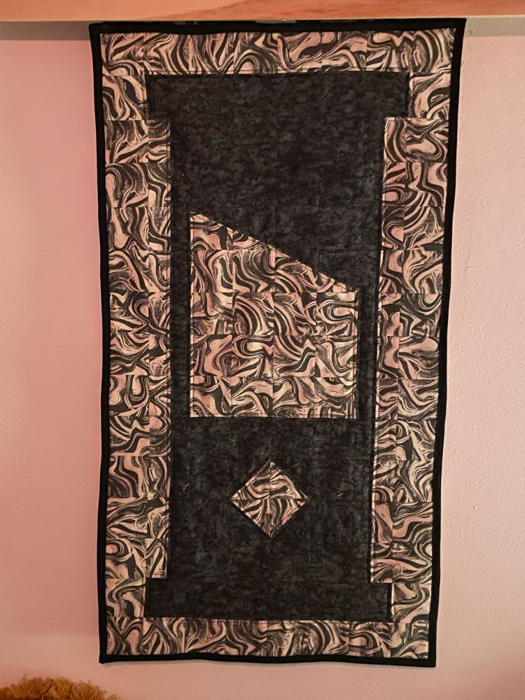 Small quilted tapestry of a black guillotine silhouette and oil spill background.