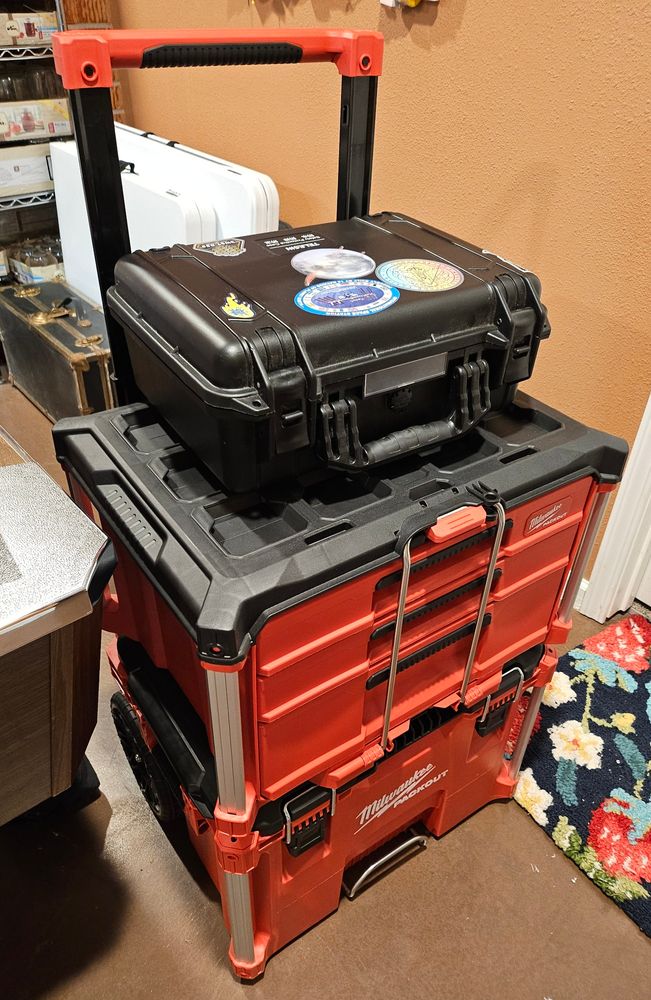 two pieces of the milwaukee packout storage containers- the modular ones with wheels on the bottom. the top container is the one with two thinner drawers and one thick drawer, which hold miscellaneous telescope tools. on top of the set is my repurposed camera hard case, which has space themes stickers on it and is now housing my 20x80 astro binoculars.