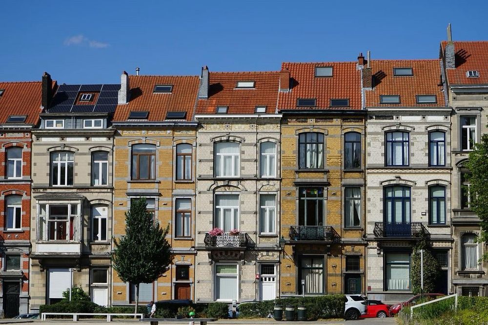 Vue sur une série de façades en briques de teintes différentes et d’inspiration Art nouveau collées l’une à l’autre. Les toits sont légèrement en escalier, compte tenu de la pente de la rue. Le ciel est tout bleu.