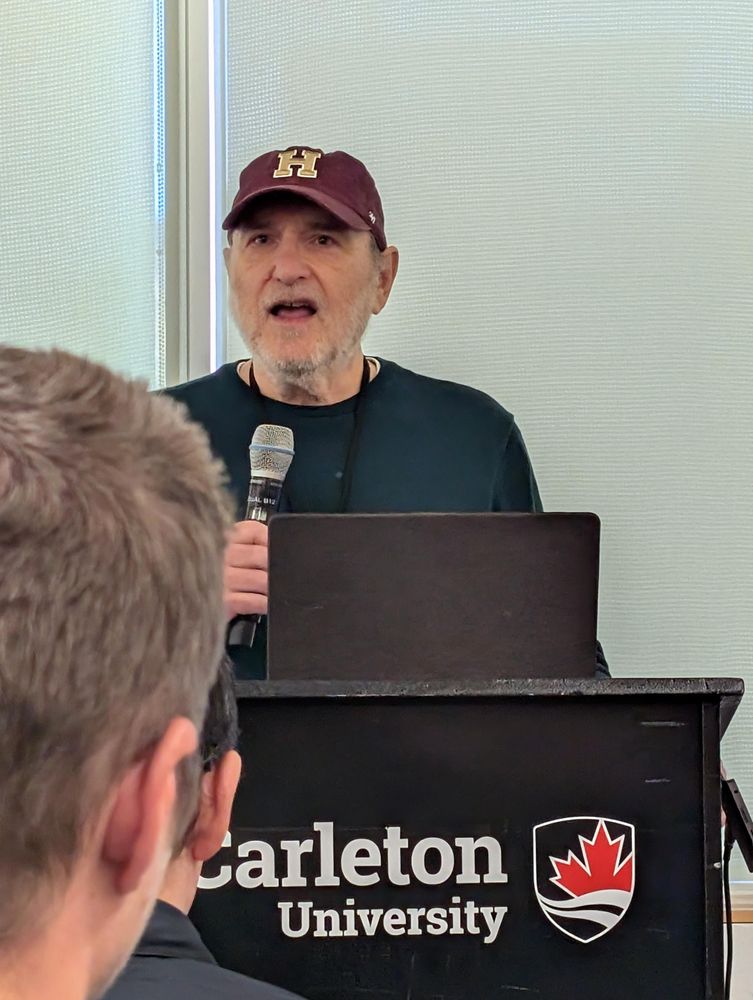 Dave Winer in a nice H hat, mic, Carleton U podium 