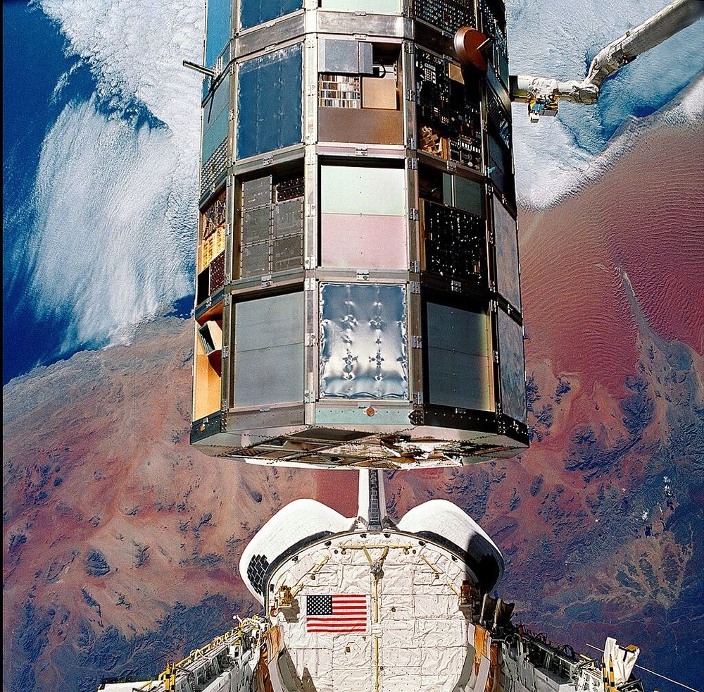 The space shuttle's cargo bay is open, the Long Duration Exposure Facility looming overhead, canada arm holding it firmly. In the background is the coast of Southern Namibia