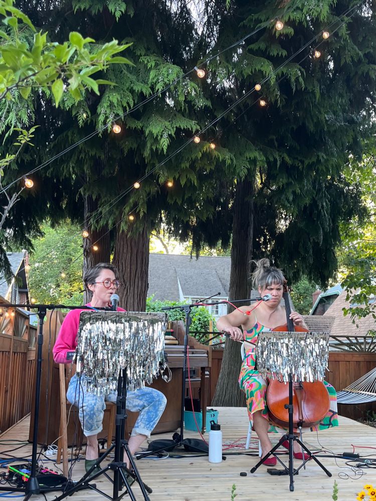 Caroline Shaw and Andrew Yee performing in a backyard, surrounded by trees. 