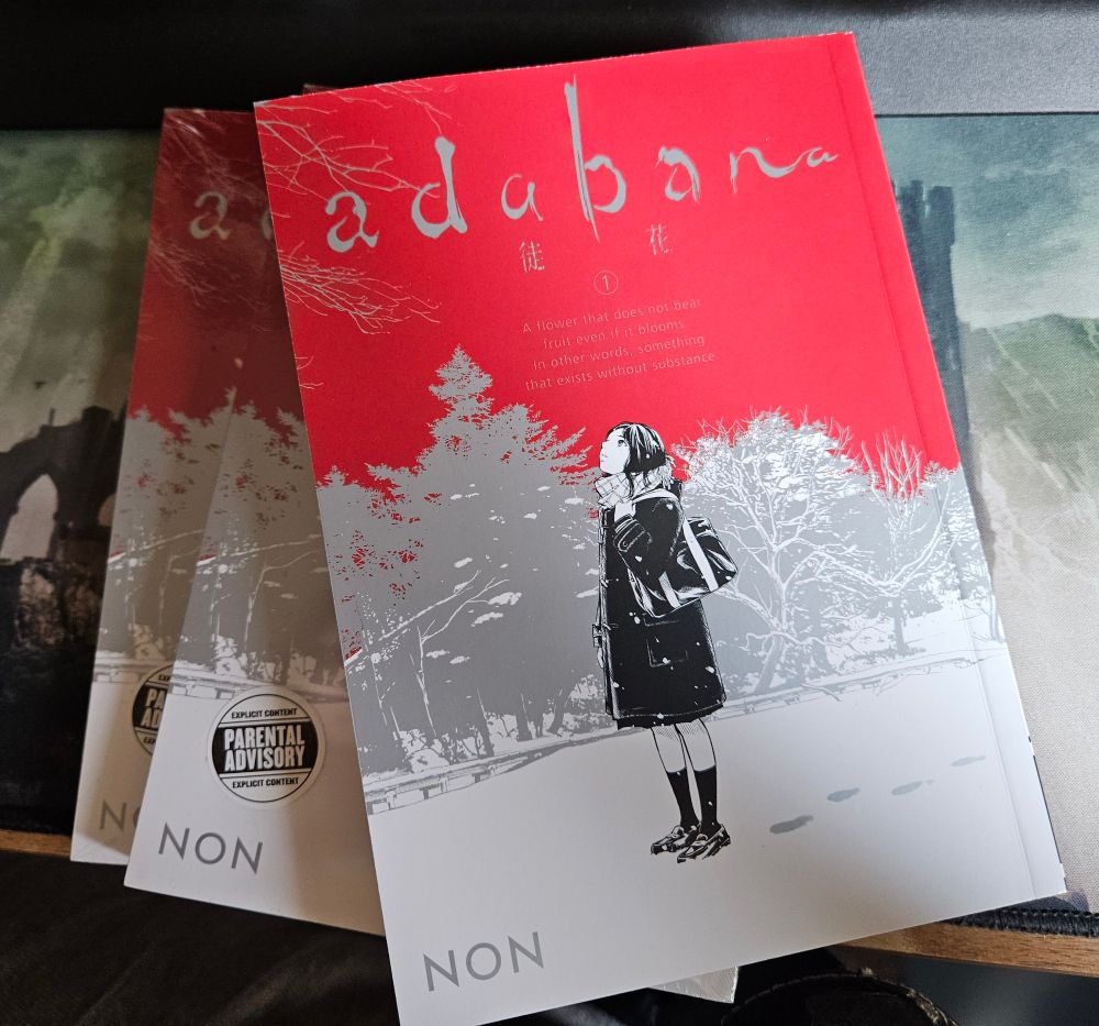 Three copies of Adabana volume 1. A girl standing in snow stares up at a blood-red sky.