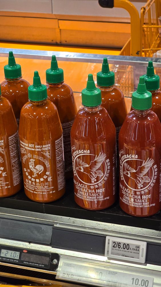 Sriracha bottles side by side in a grocery store. Both Rooster and Eagle sauce.