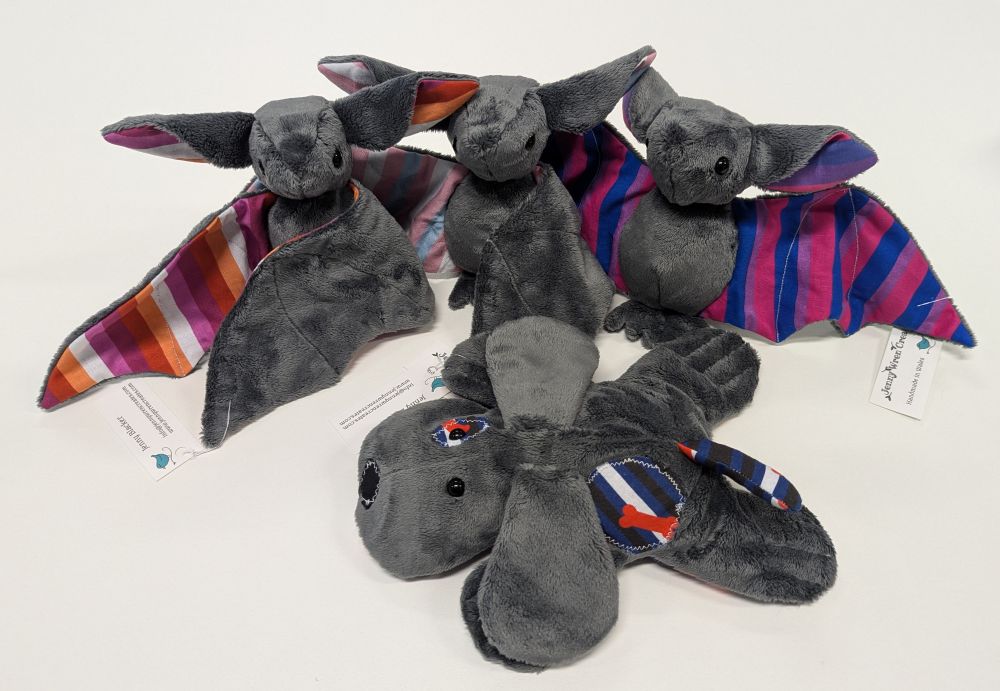 3 plush bats with pride flag wings, and one plush dog with pride patches and tail