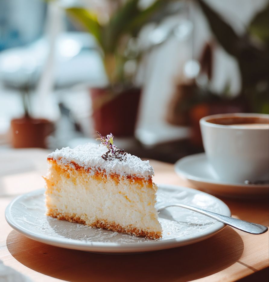 Ein stück kuchen auf einem
teller und eine Tasse im Hintergrund 