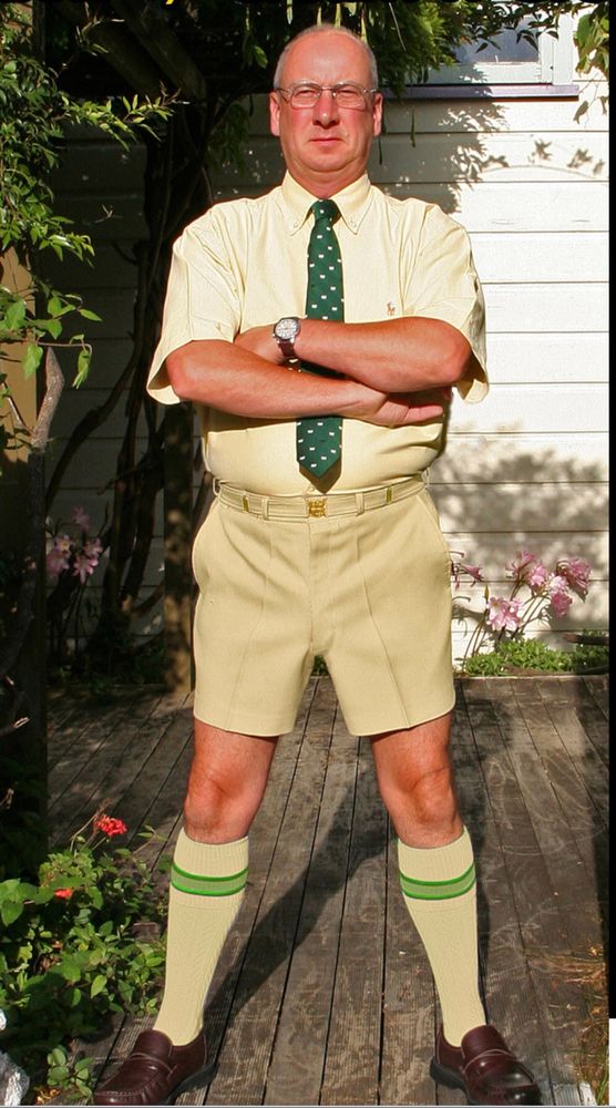 Gentleman stands proud in his walkshorts and short sleeve shirt, and tie. 