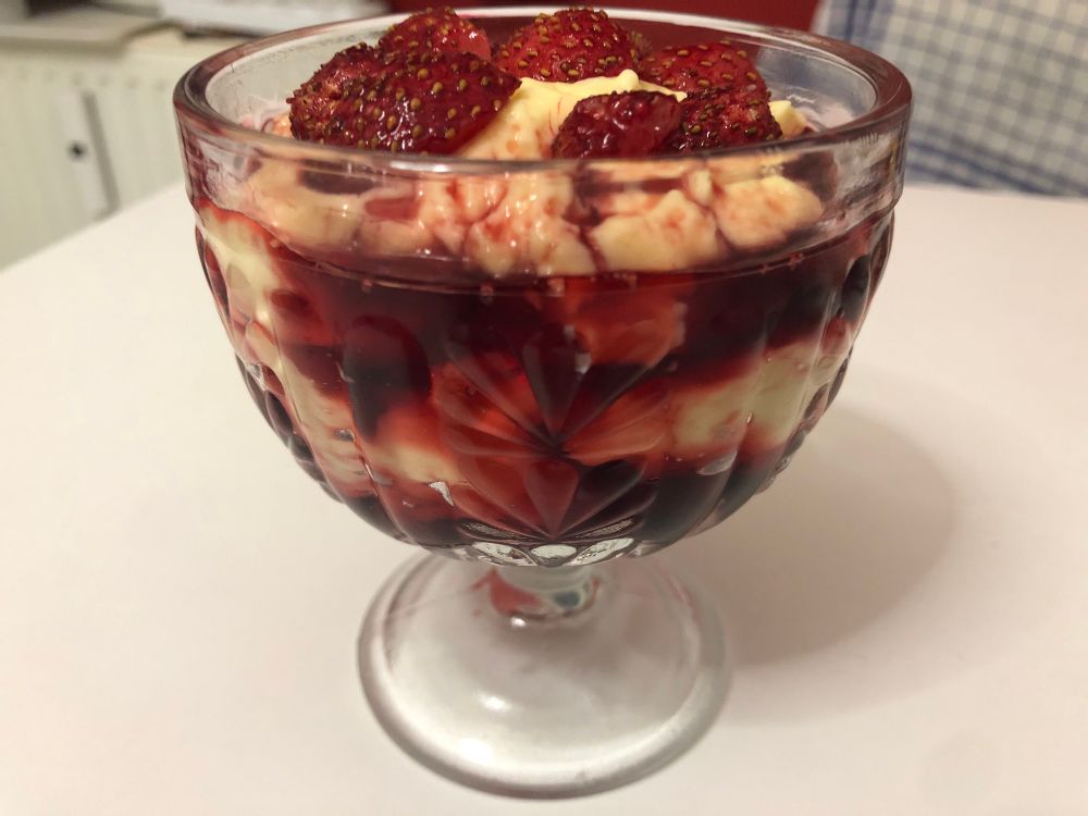 In einem Pressglaspokal geschnittene Erdbeeren in Sirup auf Vanillesahnepudding. 