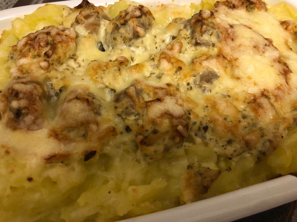 In einer kleinen Auflaufform überbackene kleine Champignons umgeben von Quetschkartoffeln. 