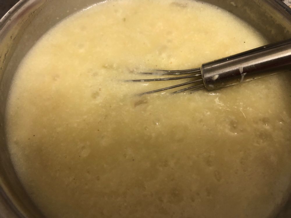 In einem mittelgroßen Edelstahltopf köchelt eine helle Sahnesauce, in der Schalottenstücke zu erkennen sind.