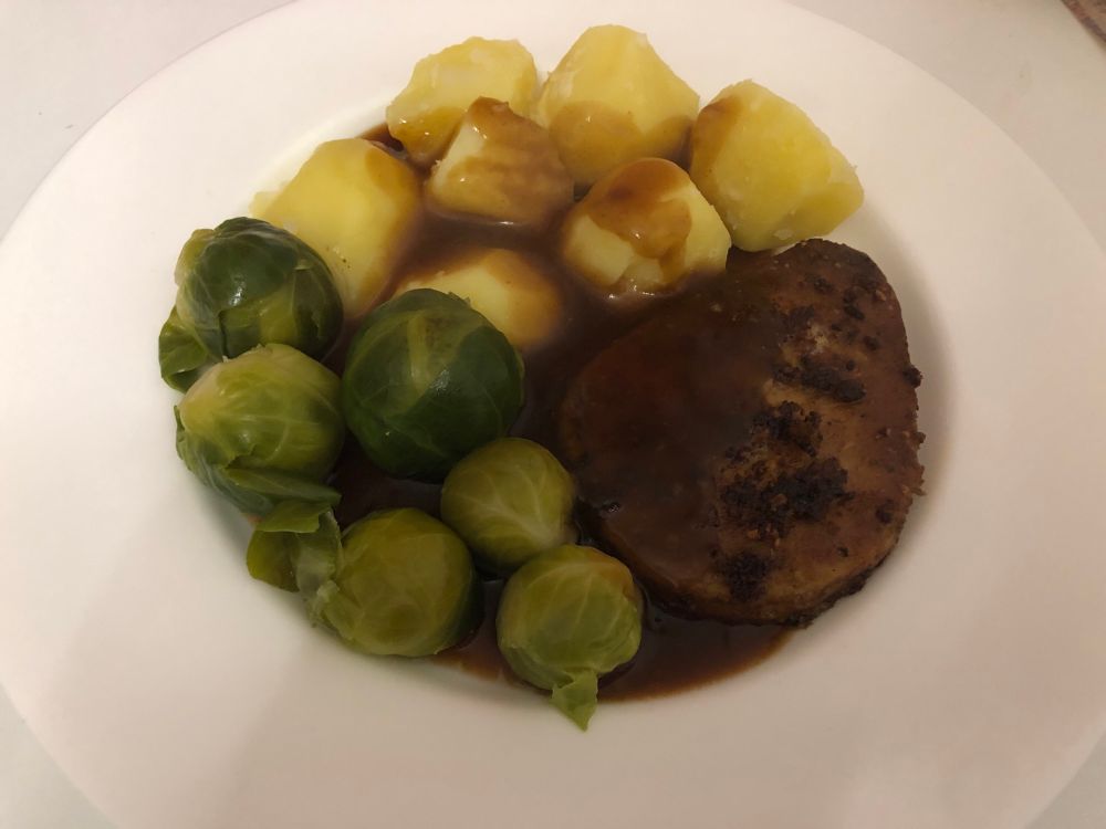 Auf einem großen runden flachen weißen Porzellanteller oben Karltoffeln, links Rosenkohl und rechts das Ersatzfleisch. Alles umspült von brauner Soße. 