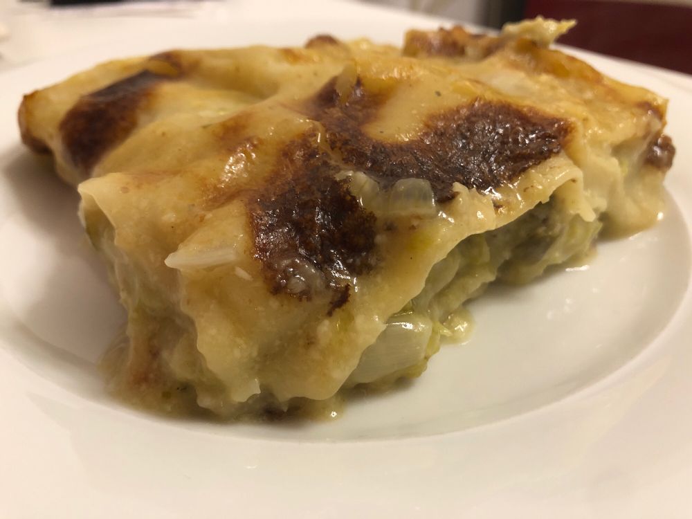 Auf einem weißen flachen runden Porzellanteller ein Stück goldbraun überbackene Lasagne.