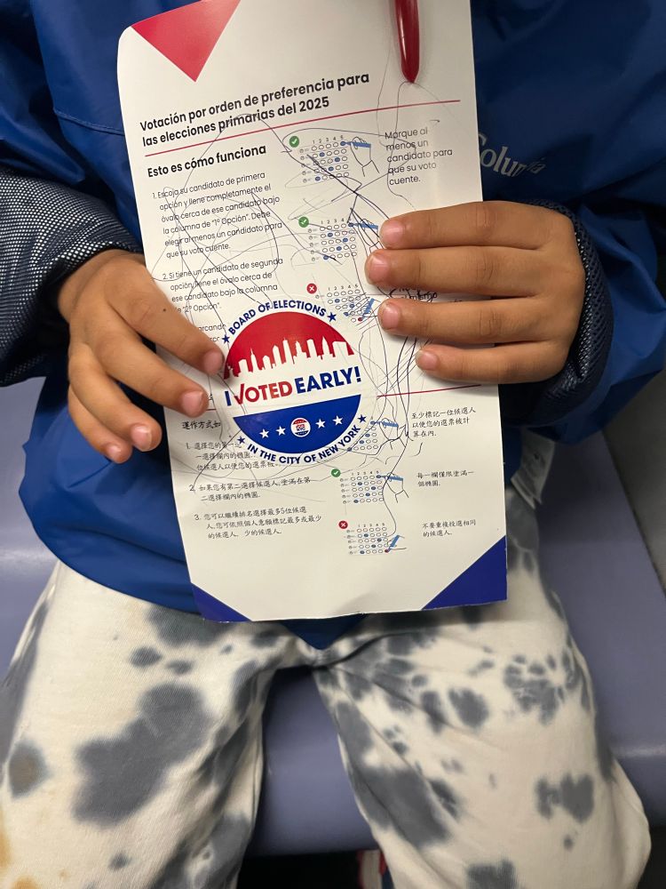 Child holds a scribbled NYC voting guide with an I Voted Early sticker on it. 