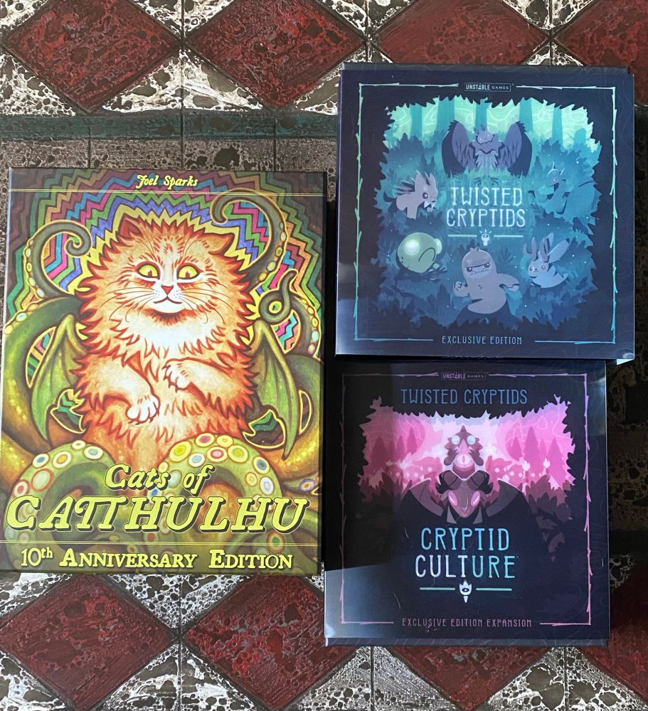 Photo of three games. Twisted Cryptids and the expansion Cryptid Culture. Cat’s of Carltthulu