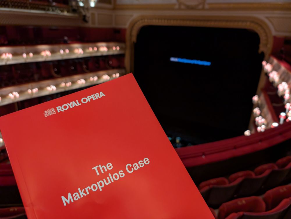 A red theatre programme with text reading "Royal Opera. The Makropulos Case". The background is a slightly blurred view of the Royal Opera Horse as viewed from the amphitheatre.