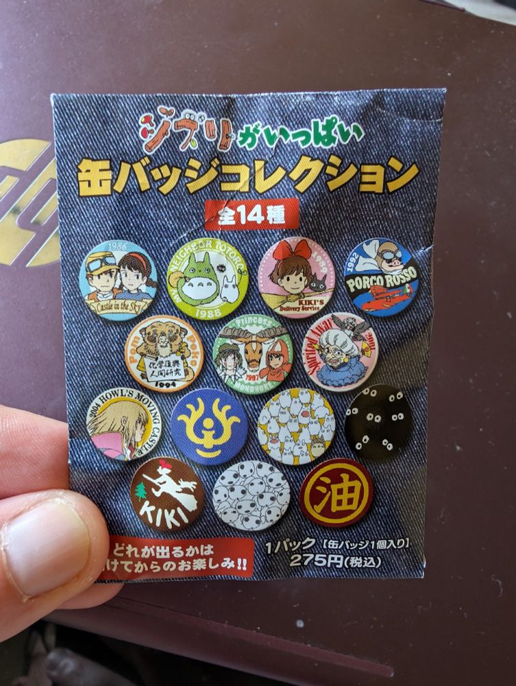 A paper pouch printed to look like denim and showing the designs of twelve badges inspired by Studio Ghibli films.
