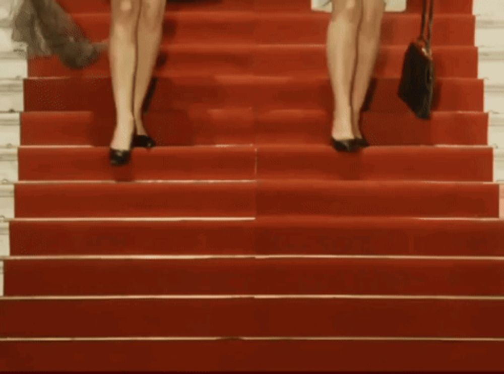 two women walking down red carpeted stairs with a black purse